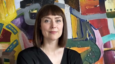 Kvinna med mörkt halvlångt hår står framför tavla. 