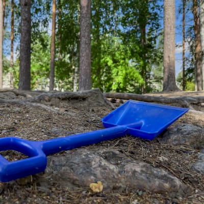Sininen leikkilapio maassa etualalla, taustalla puita.