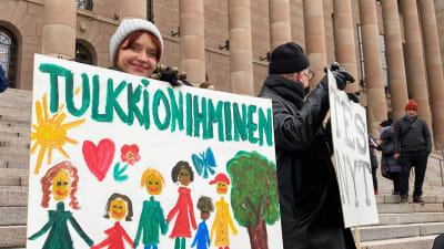 Alice Jalonen håller en skylt med texten "Tulkki on ihminen" på riksdagens trappa.