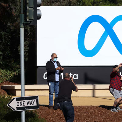 Några människor står vid Metas högkvarter och tar selfies och bilder av logotypen utanför byggnaden.