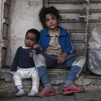 Två små barn sittande bland skräpet på en gata.