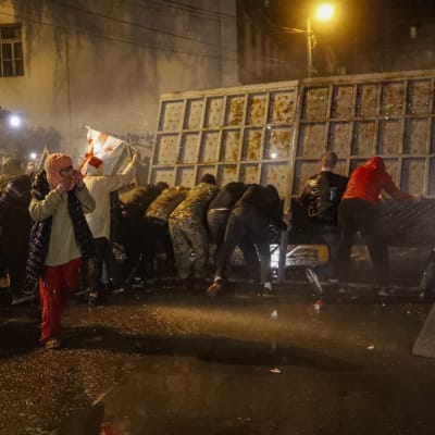 Demonstranter tar skydd bakom en barrikad.