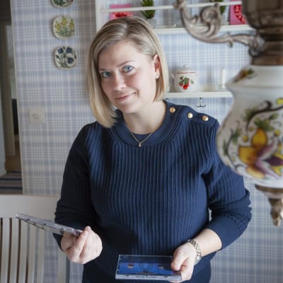 Madeleine Roos i blå tröja, hemma i sitt kök, hon håller i två cd-skivor och har blont hår