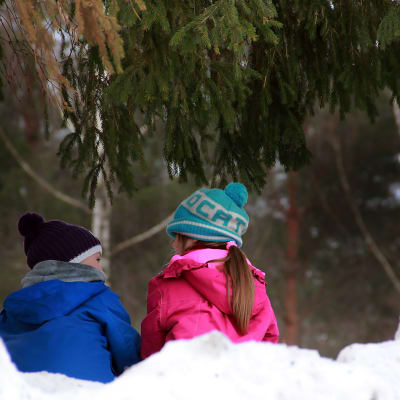Två barn sitter i en snödrivar och pratar.