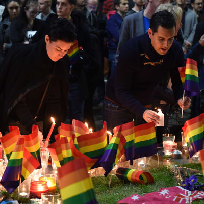 Två personer tänder ljus och placerar regnbågsflaggor bredvid flera regnbågsflaggor vid Taylor Square, i Sydney, Australien. Flera sydneybor samlades för en tyst solidaritetsdemonstration för offren i Orlando.