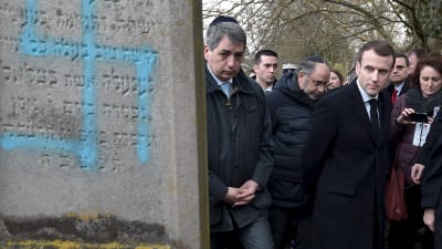 Emmanuel Macron bredvid en judisk grav som någon målat ett hakkors på.