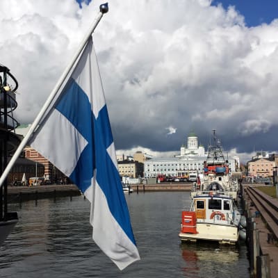 En finsk flagga syns i förgrunden. I bakgrunden Helsingfors.