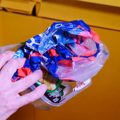 Hand som lägger plast i ett avfallskärl.