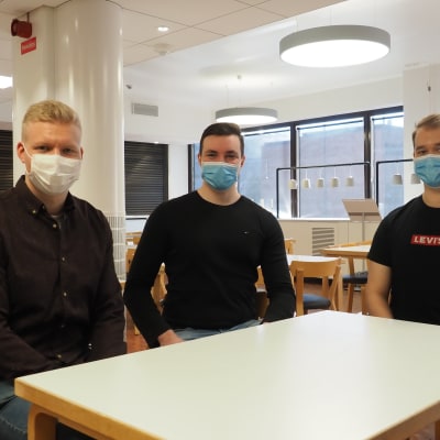 Kolme opiskelijaa istuskelee yliopiston aulassa.