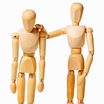Två träfigurer. En tröstar den andra.