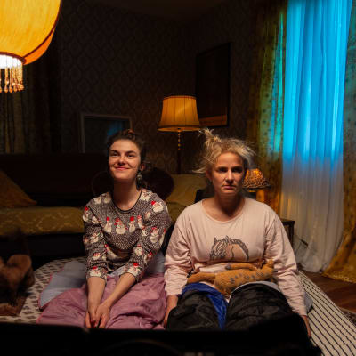 Safin universumissa näyttelevät Safi (Johanna Öhman) ja Riikka (Emilia Jansson) istuvat patjojen päällä lattialla.