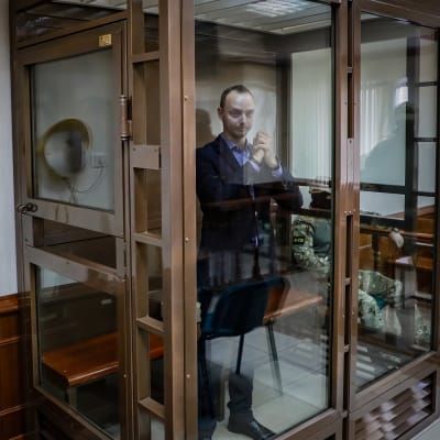 Ivan Safronov i en glasbur under rättegången. På ömse sidor om glasburen finn camouflageklädda och beväpnade vakter.