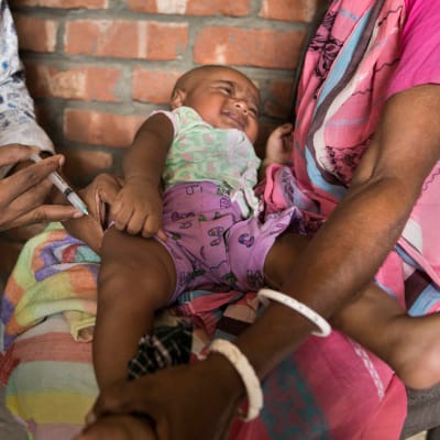 Ett litet barn vaccineras i Indien. Barnet ligger i mammans famn.