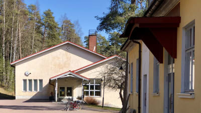 Ett beige skolhus med två cyklar parkerade framför. I förgrunden syns fasaden på en annan byggnad.