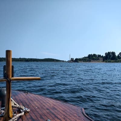 Vy över fästningsön Svartholm från en träbåt. Det är soligt och sommar.