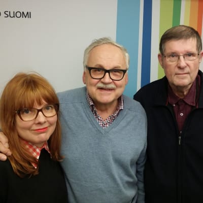 Susanna Vainiola, Ismo Sajakorpi ja Fredi seisovat Radio Suomen seinän edessä