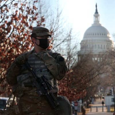 Två kamouflageklädda militärer med munskydd spanar med kongressens vita kupol i bakgrunden.