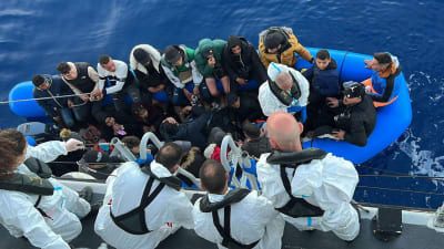 Räddningspersonal böjer sig över relingen mot en gummibåt med flyktingar 