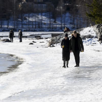 En man och en kvinna promenerar i solskenet på en isig strand.