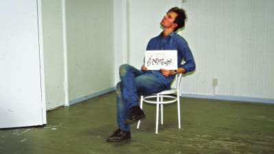 Mecki Andersson istuu tuolilla tyhjässä huoneessa vuonna 1986, sylissään kyltti: After Eight