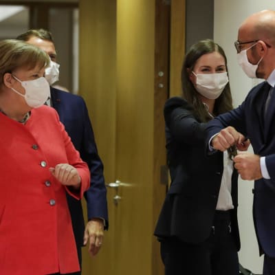 Sanna Marin armbågshälsar med Charles Michel. Tysklands förbundskansler Angela Merkel tittar på från sidan. Alla är iklädda munskydd.