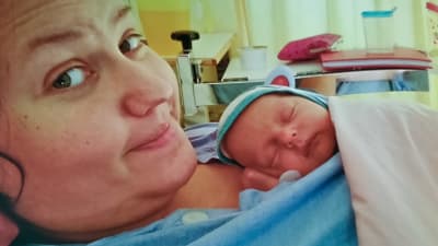 Daniel ligger i en sjukhussäng med sitt nyfödda barn på bröstet. Båda riktar ansiktet mot kameran men babyn sover.