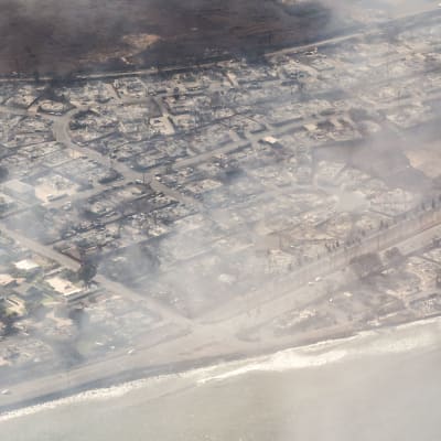 Flygbild av staden Lahaina på Maui efter en stor brand som förstörde största delen av staden. Rök syns sväva över staden.