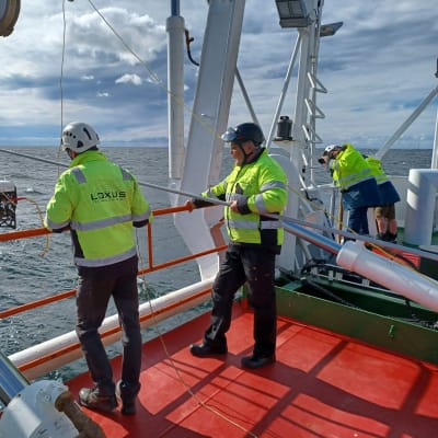 Män på däck sänker ner apparat från forskningsfartyg ute till havs. 