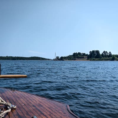 Vy över fästningsön Svartholm från en träbåt. Det är soligt och sommar.