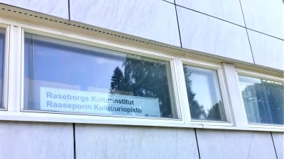 Ett fönster där man ser en skylt med texten: Raseborgs kulturinstitut, Raaseporin kulttuuriopisto. Vita marmorväggar.