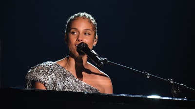 Alicia Keys sitter vid ett piano och sjunger i en mikrofon. 