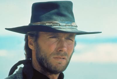 Lähikuvassa parrakas Clint Eastwood päässään musta nahkainen lierihattu katsoo sirmät sirrillään jonnekin kameran ohi, taustalla pilvistä taivasta, kuva elokuvasta Ruoska eli High Plains Drifter.