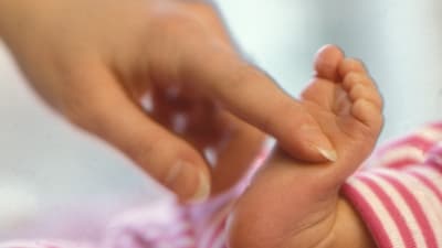 En vuxen kvinnohand kittlar en nyfödd under foten