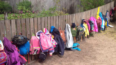 Skolväskor och jackor hänger på ett staket på eftisgård.