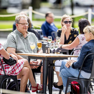 Tre personer sitter runt ett bord på en uteservering.