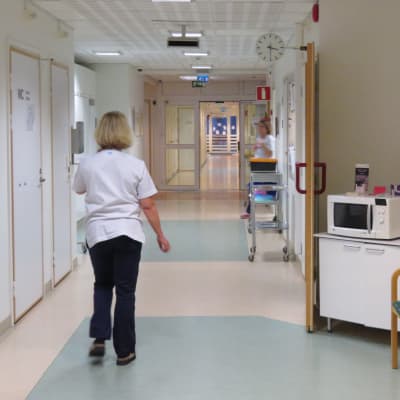 En kvinna, sjukskötare med ryggen mot kameran går längs en korridor i Raseborgs sjukhus.