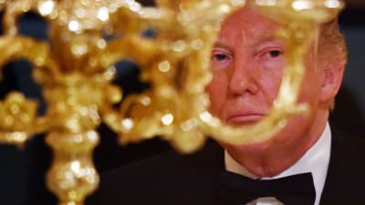 Fotografi med glimten i ögat. President Donald Trump bakom stor gyllene ljusstake.
