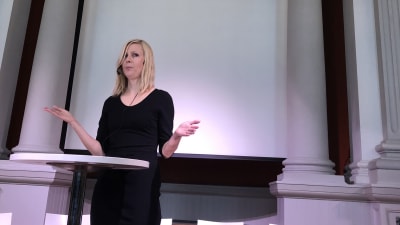 Jessikka Aro talar vid sin bokpublicering, under väggtexten: "Herran pelko on viisauden alku"