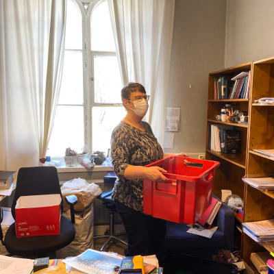 En kvinna håller i en röd flyttlåda inne på ett kontor.
