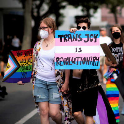 Människor protesterar för transpersoners rättigheter. De ropar och håller upp skyltar.