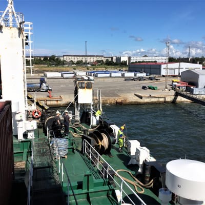 Ett fartyg anlöper hamn i Paldiski i Tallin. Sommar, blå himmel. Fotograferat från båten mot hamnen. Ganska tomt på folk, bilar och annat i hamnen.