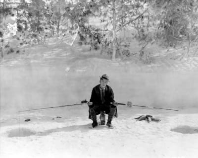 Buster Keaton istuu pilkillä kitaran päällä käsissään kaksi pitkää vapaa. Kuva elokuvasta The Frozen North eli Kylmä Pohjola/Busterin seikkailut pohjoisnavalla