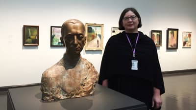 Kvinna bredvid en skulptur i en utställningssal.