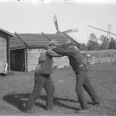 Två män leker "kragtag", där man håller i sin motståndares krage och försöker fälla denna på rygg. Bilden är tagen 1930 i Korsnäs kyrkby.