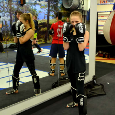 En kvinna står med boxningshandskarna framför ansiktet framför en spegel.