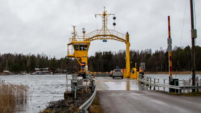 En gul färja vid färjfäste. Två bilar har just kört på färjan.