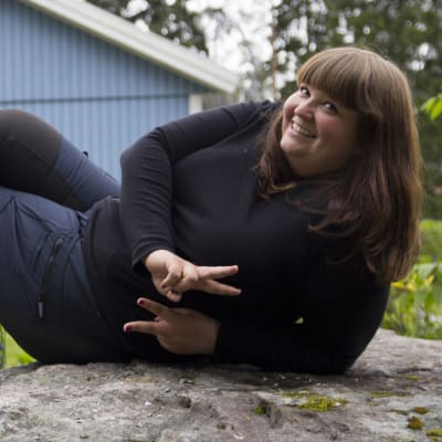 Kristine Vesterlund  poserar liggand epå en stor, grå sten. 