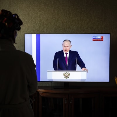 En kvinna tittar på den ryska presidenten Vladimir Putins tv-tal inför federala församlingen, i Moskva.
