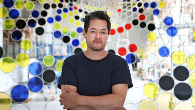 Jacob Hashimoto, en artist står med armarna i kors framför ett konstverk med färggranna cirklar.