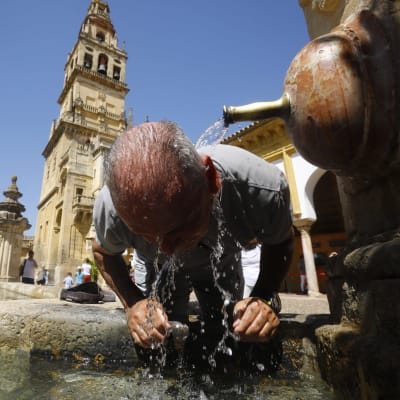 En äldre man svalkar sitt huvud vid en fontän för att kyla ner i hettan.